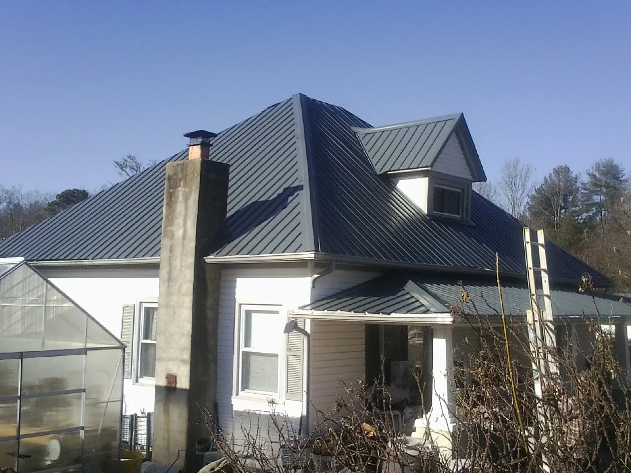 Dark blue standing seam metal roof on a white farmhouse with dormer — Slate & Tile Roof Repair by Roofing Brothers in Isanti