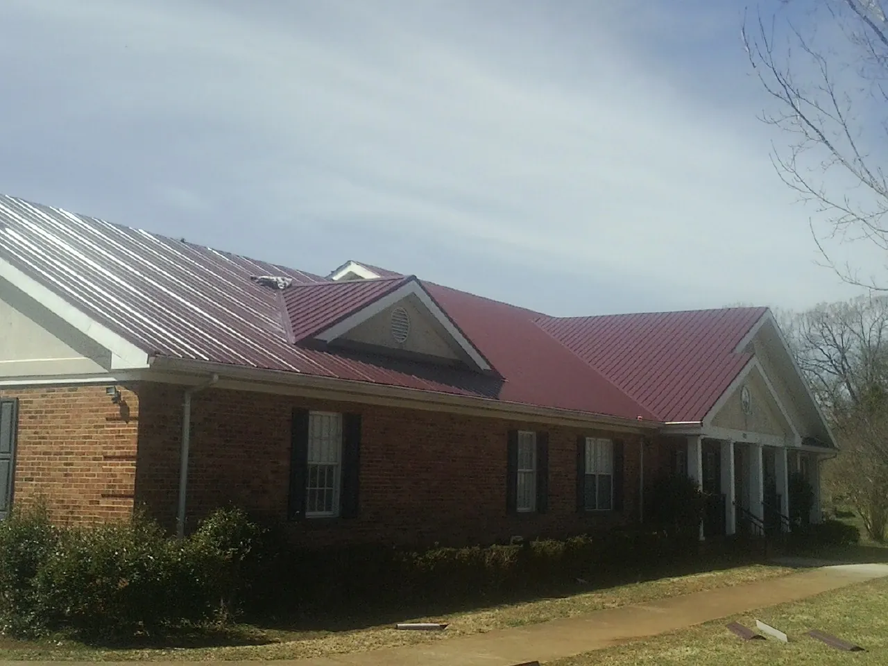 Red metal roof with gabled entries on a long brick building, from a Hail Damage Roof Repair job in Isanti