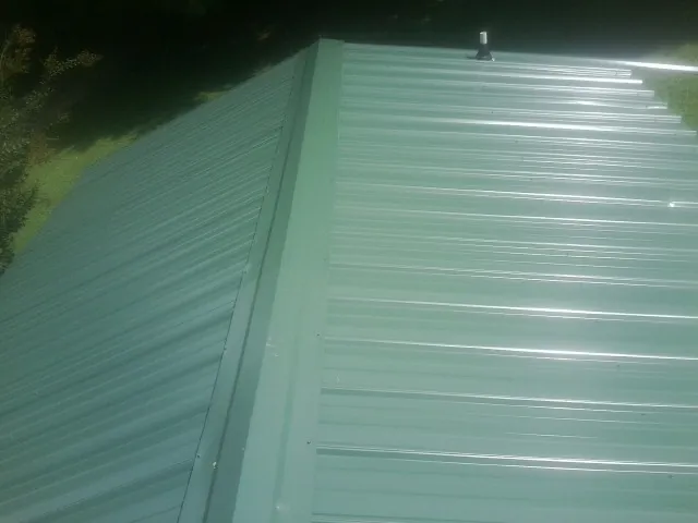 New green metal panels meeting at the ridge of a roof — Flat Roof Repair work by our crew in Isanti