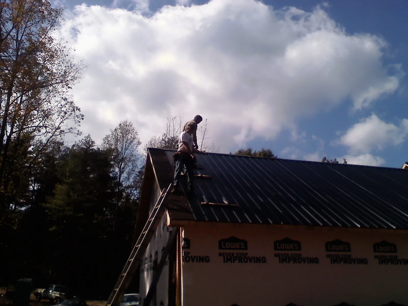 Roofer fastening dark metal panels high against a cloudy sky, from a Roof Inspection job in Isanti