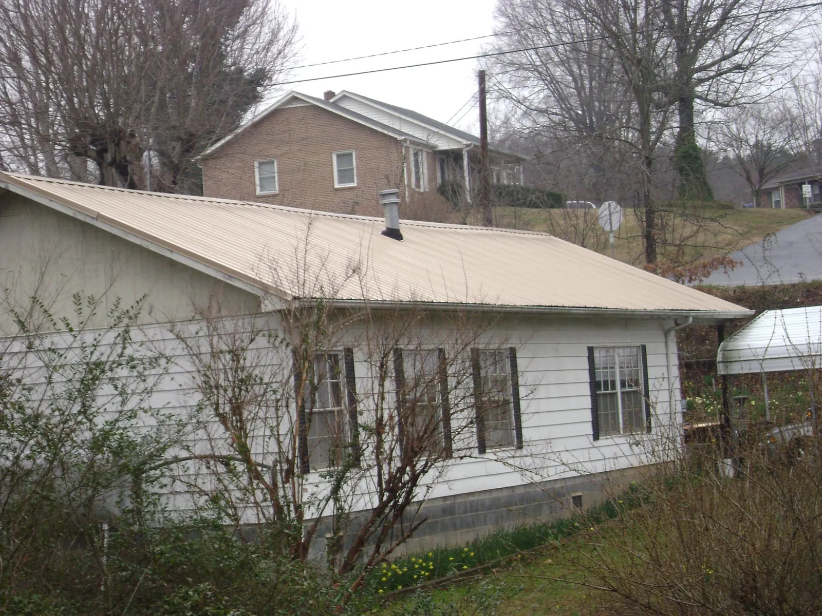 Tan metal roof on a white sided house set into a hillside — Commercial Roofing by Roofing Brothers in Isanti