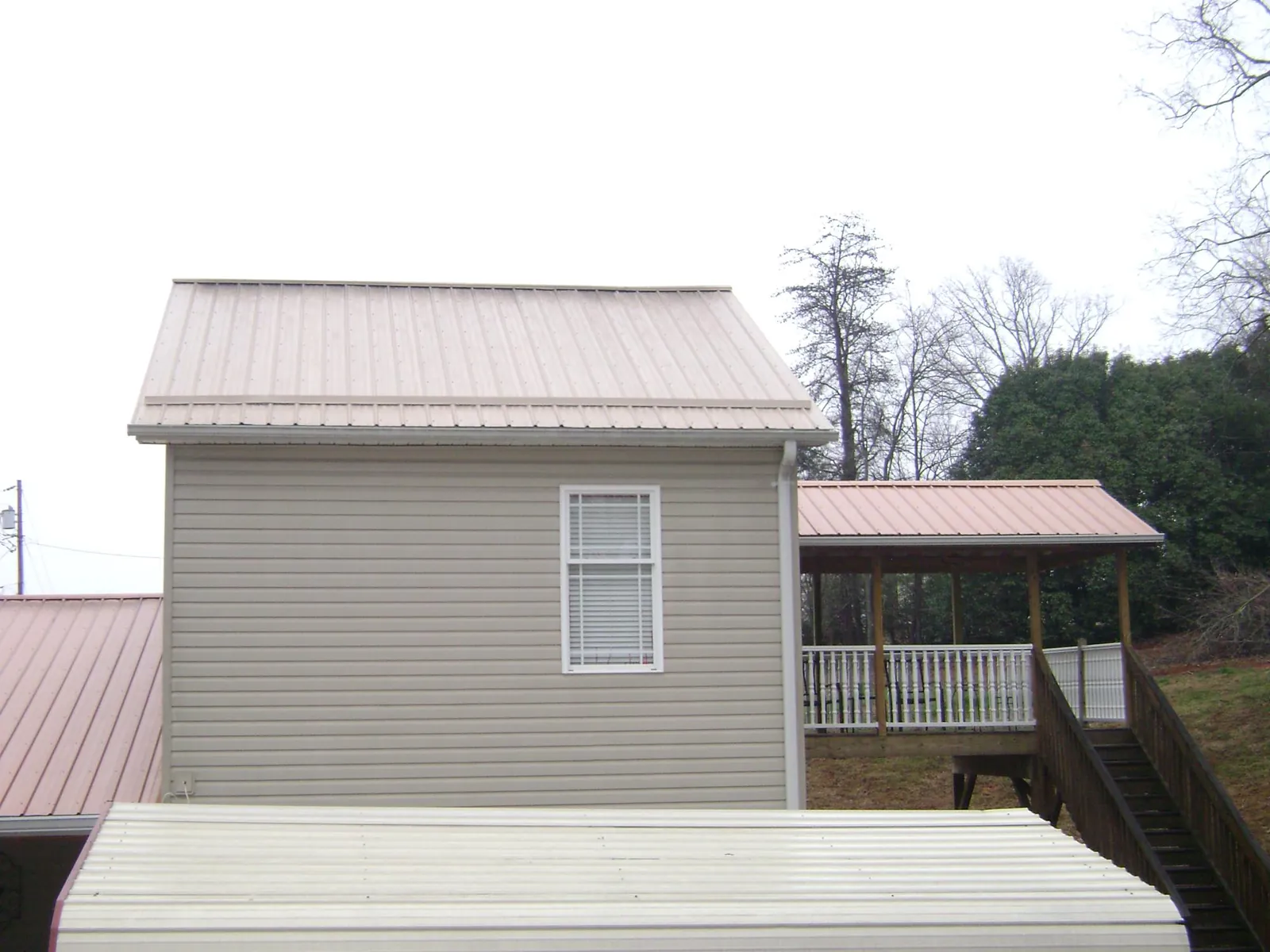 Tan metal roofs on a two story addition and attached porch, from a Roof Replacement job in Isanti
