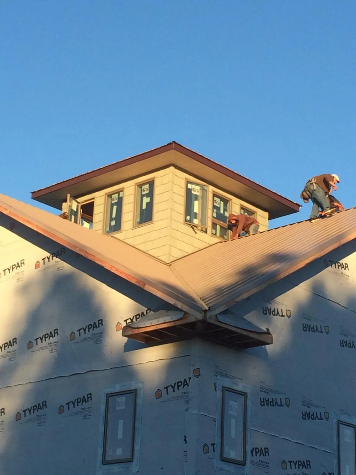 Roofers working around a rooftop cupola on a new metal roof at sunset — Roof Waterproofing in Isanti by Roofing Brothers